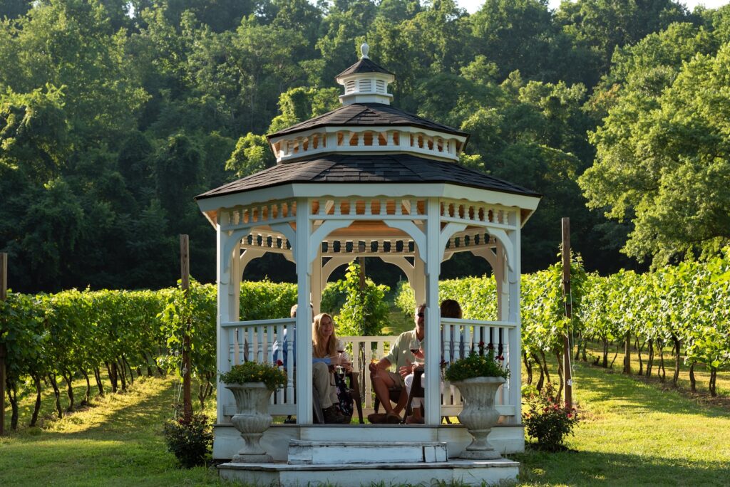 Looking for romantic weekend getaways in Virginia? Explore wine country, tastings, and elegant boutique hotels for couples.A photo of couples enjoying a glass of wine in a gazebo near a vineyard in Virginia