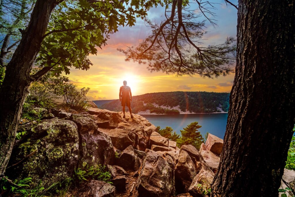 A silhouette of a man looking out into the sunset over Devils Lake State Park from a hiking viewpoint in Baraboo, Wisconsin USA.