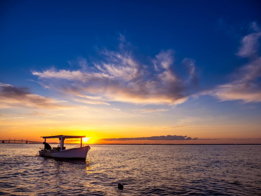 A horizontal photo of a Chesapeake Bay waterman crabbing at sunrise using a traditional crab boat.