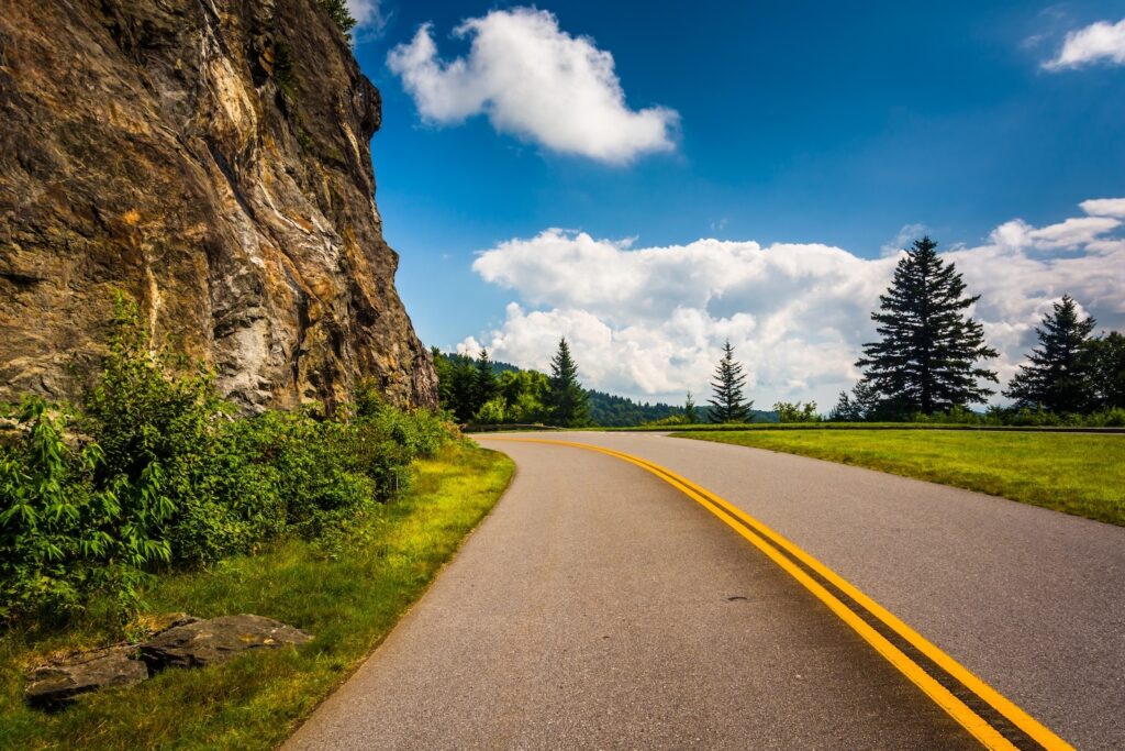 Driving the Blue Ridge Parkway is one way to visit North Carolina mountain towns. Here the road bends to the left around a mountain face.