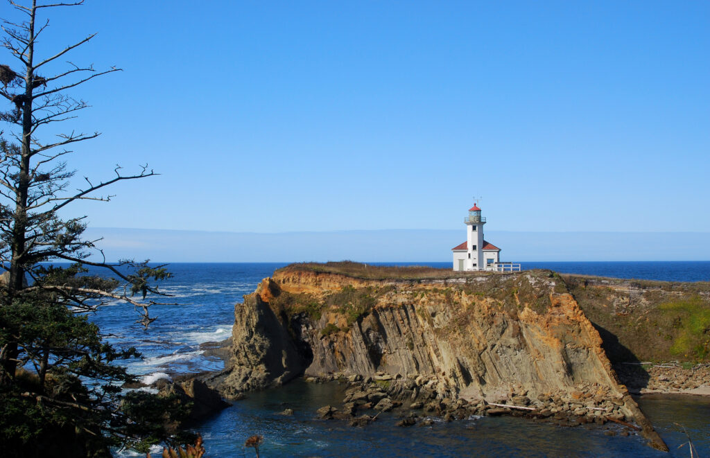 The Lighthouse perched high on the rocks, blue sky day, Pacific Ocean on the background at Cape Arago State Park