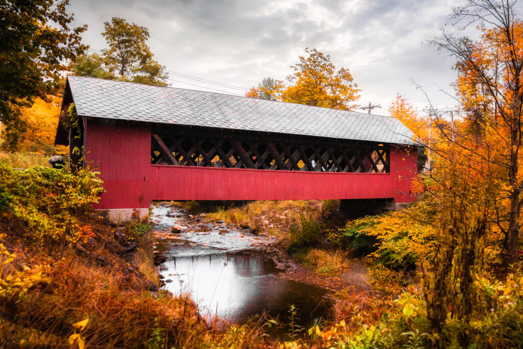 Vermont covered bridge over river, surrounded by fall foliage.