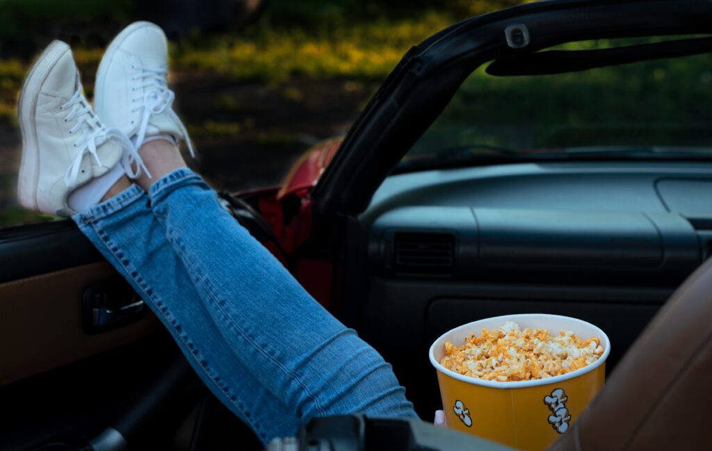 Attend a movie at the Brazos Drive In for nostalgic fun. Woman in convertible with popcorn.