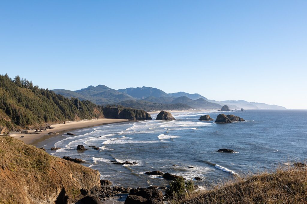 Sunny day at Ecola State Park with stunning views of mountains and ocean waves crashing against the rocky coastline. A perfect spot to appreciate the beauty of the Pacific coast