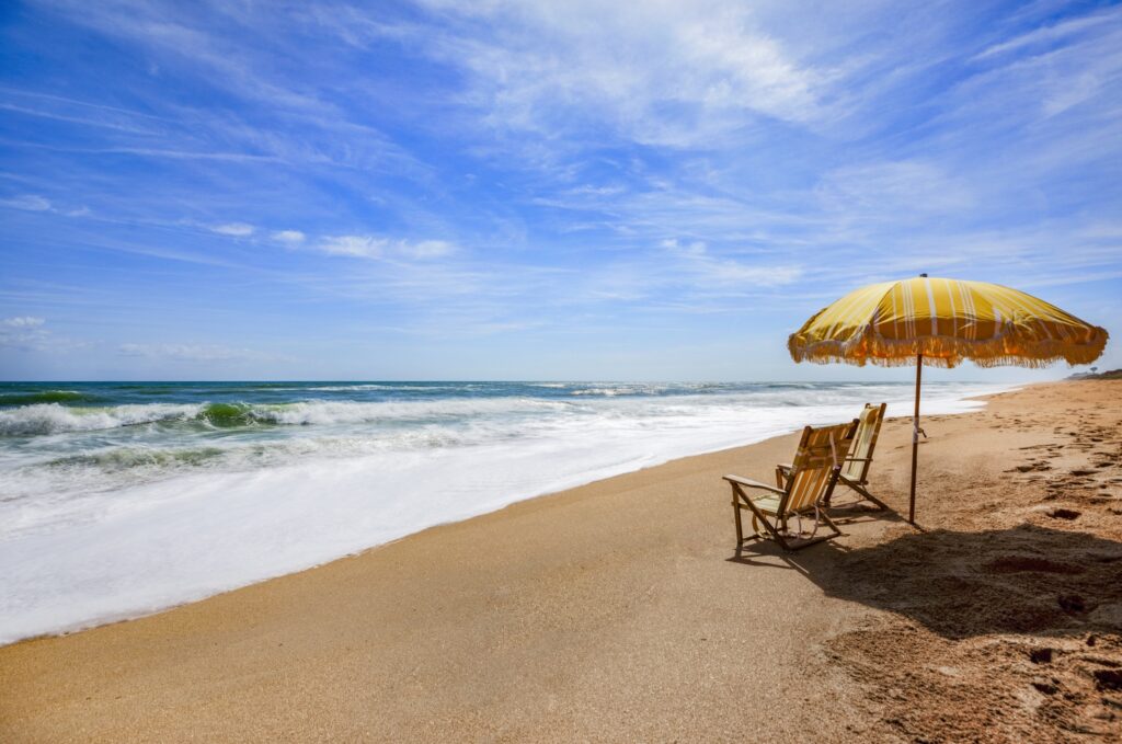 Yellow and white striped beach umbrella and matching beach chairs on Flagler Beach, one of the best hidden romantic getaways in Florida.