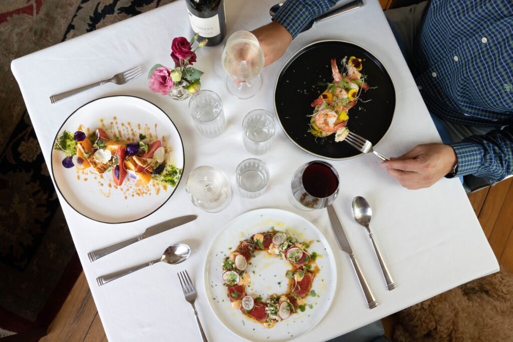 A table scape for three at a fine dining restaurant, with bottles of wine, flowers and upscale dishes, at one of the best Exeter NH restaurants.