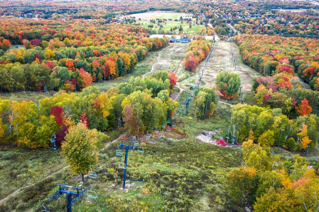 Beautiful aerial view looking down one of the ski runs at Rib Mountain in the autumn season with Wisconsin fall colors of bright red, orange and yellow colored foliage on the trees lining the runs and chair lift.