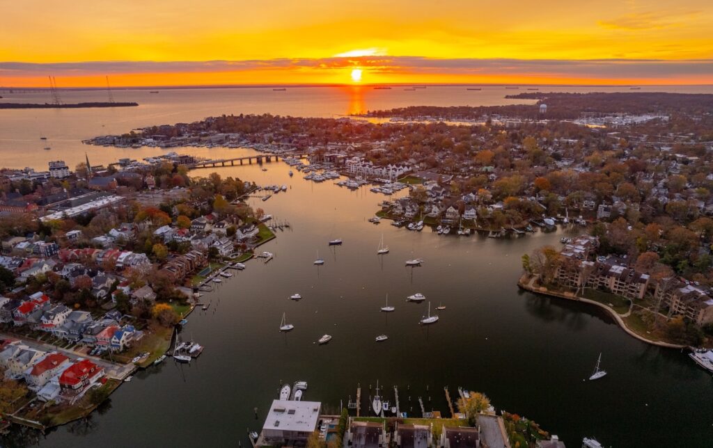 Experience the best things to do in Rock Hall MD in the fall like this aerial shot of a harbor and Chesapeake Bay at sunset, showing fall leaves, boats, and water.