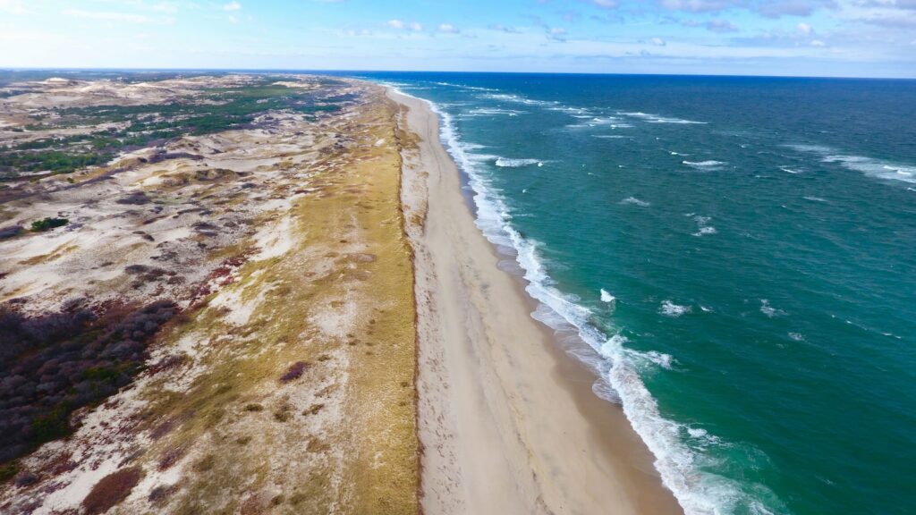 An aerial view of the Cape Cod National Seashore, showcasing the grass, dunes, sand, and sea.