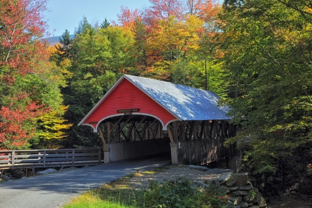 A red covered bridge surrounded by New Hampshire fall foliage.