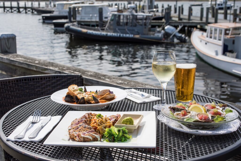 Three plates of seafood with wine and beer by the ocean at one of the Cape Cod restaurants on the water.