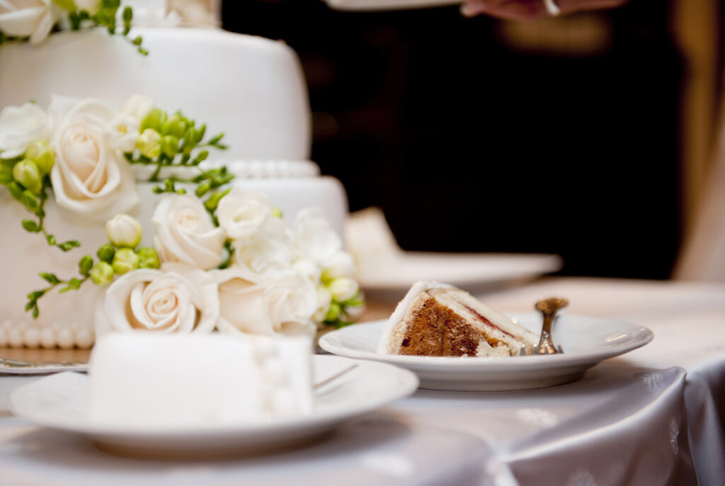 Wedding Cake with white flowers and green leaves, slice on plate. how to plan a wedding in Stillwater MN