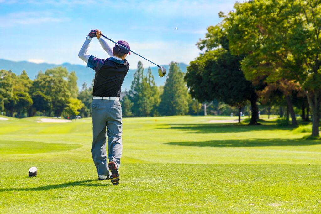 Golfer, facing away from camera, taking a swing on the green at Bailey Creek Golf Course in the shadow the mountains near Lassen.