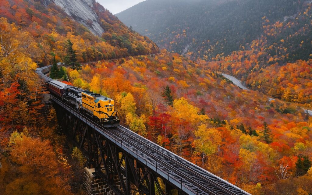 The Conway Train on the tracks in the mountains surrounded by fall foliage at the Conway Scenic Railroad in New Hampshire.
