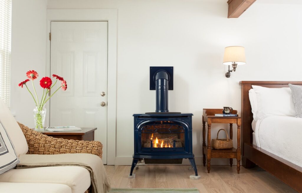 A fireplace next to a night stand, bed, and seating area in a guest room at the best Bed and Breakfast in New Hampshire.