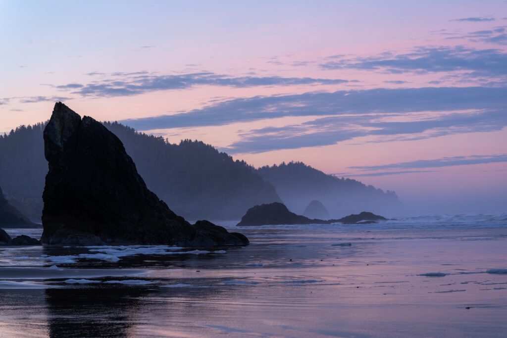 Arch Cape Oregon sea stacks silhouetted against a pink sunset over the beach