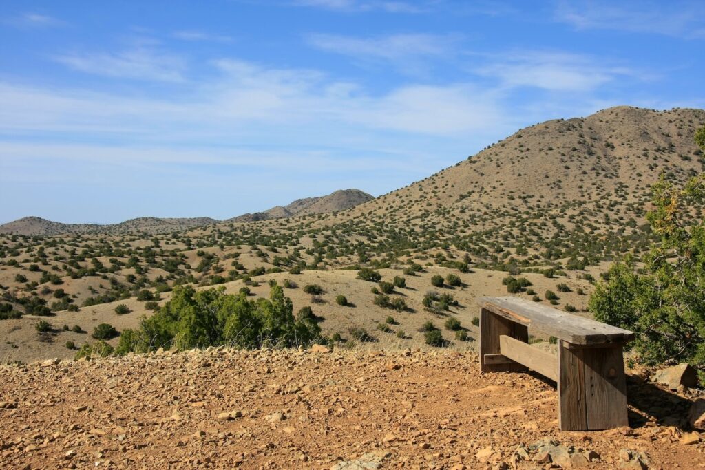 A wooden bench on a summit in Cerrillos Hills State Park with surrounding mountains.